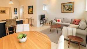 A modern living room with a wooden dining table, a sofa, a TV, and a painting on the wall. - The Elm Coach House (Chipping Norton)