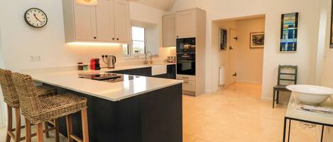 A modern kitchen with a large island, pendant lights, and a dining area with wicker chairs.
