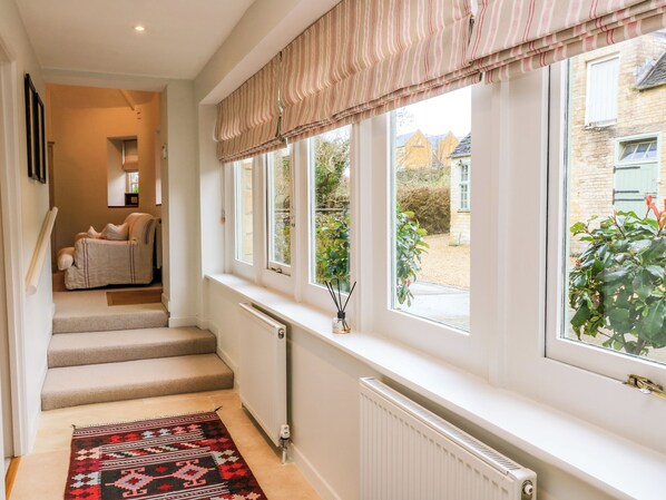 A staircase leading to a landing with a radiator, a window with striped valance, and a view of the outside. - The Elm Coach House (Chipping Norton)