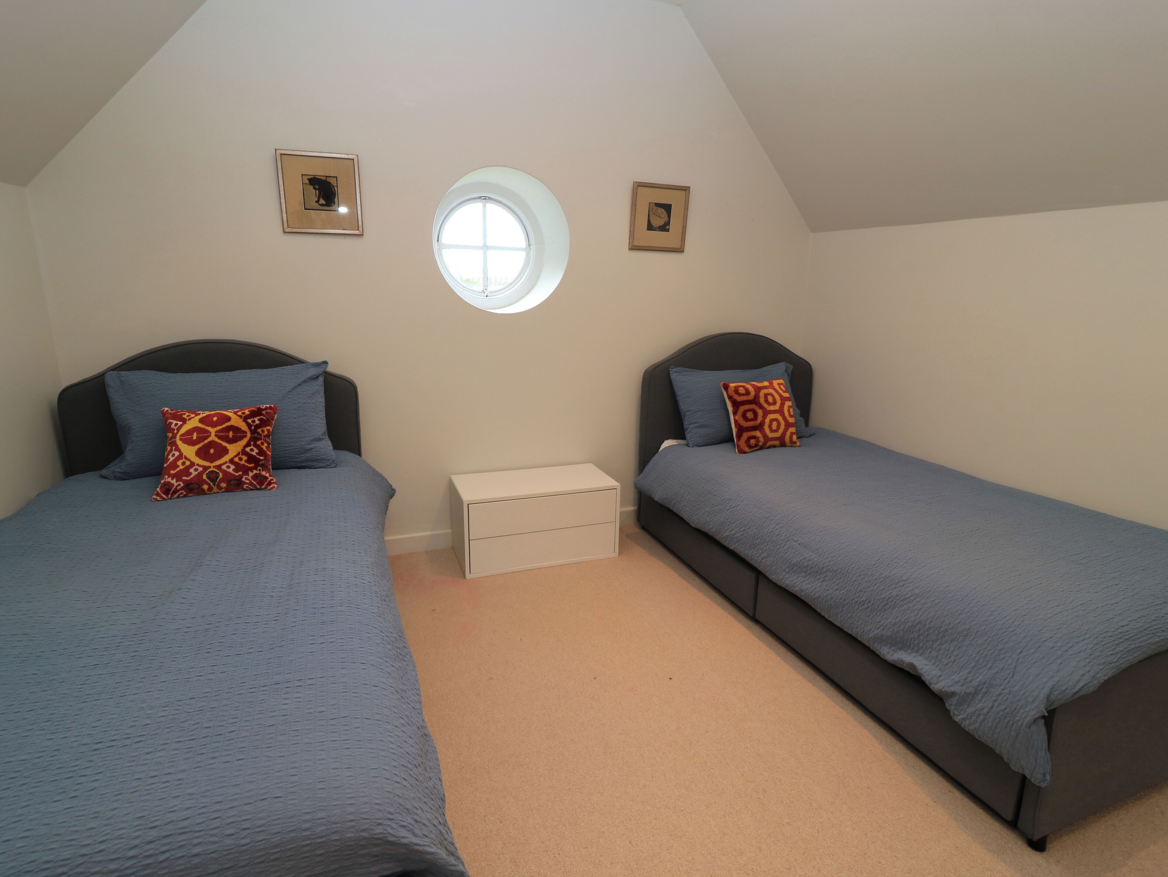 A bedroom with two beds, a small window, and two framed pictures on the wall.
