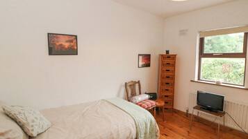 A bedroom with a bed, a chair, a TV on a stand, a window, and a wooden cabinet.