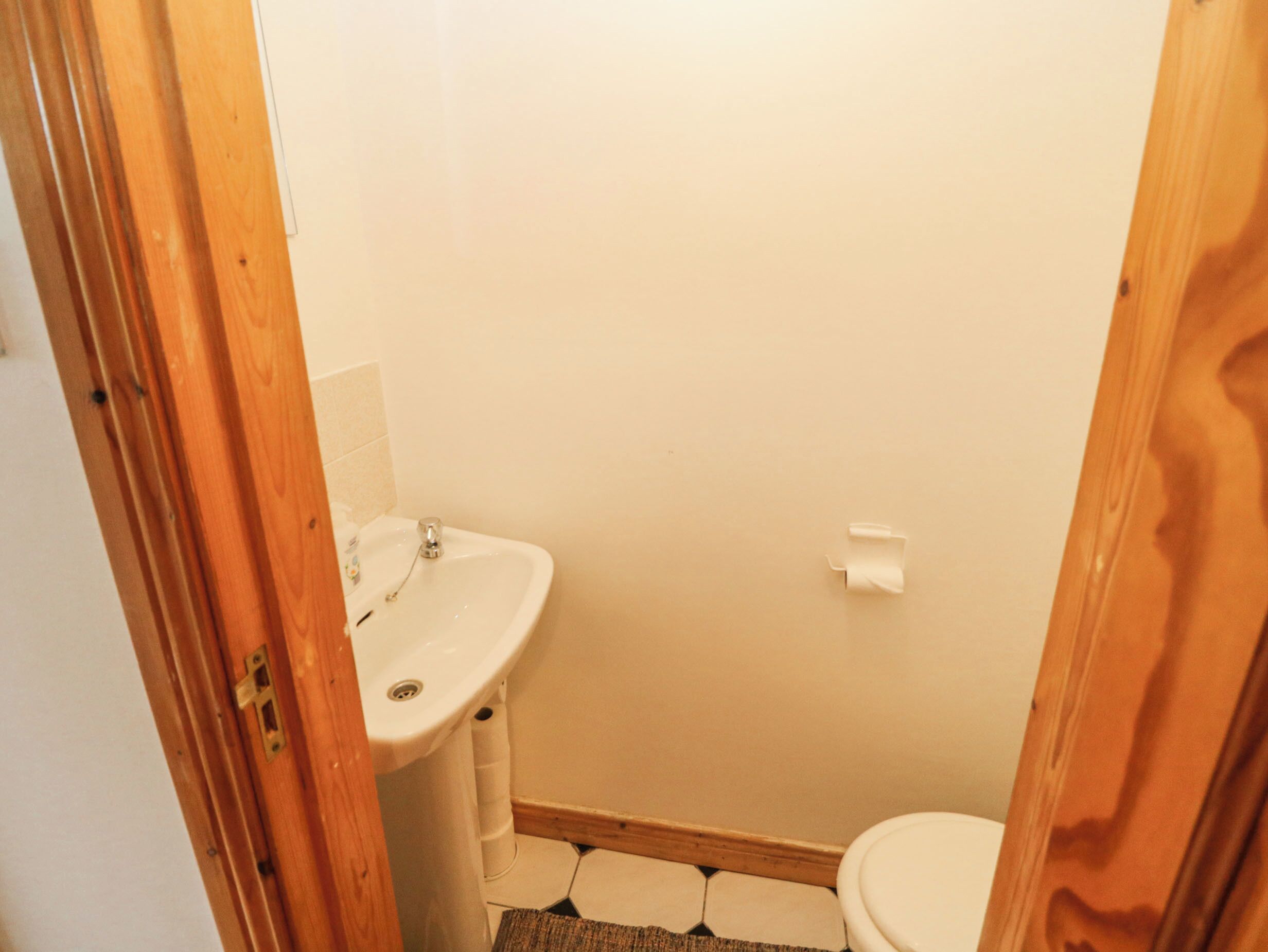 Une petite salle de bain avec un lavabo blanc, des toilettes et un cadre de porte en bois.
