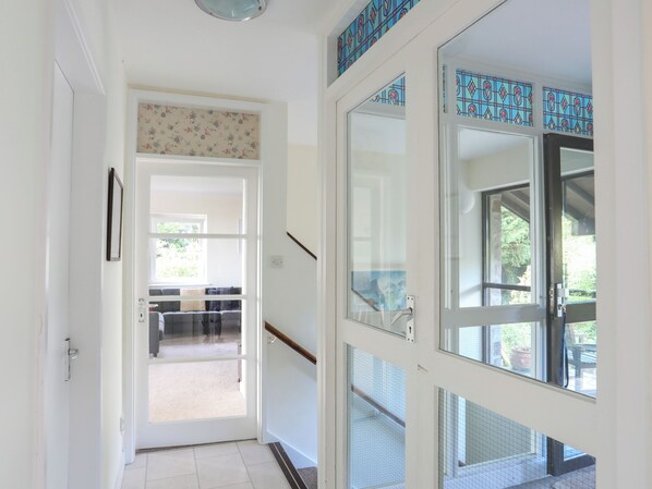 A hallway with a glass door leading to a balcony with a view of greenery. - The Wellington (Pwllheli)