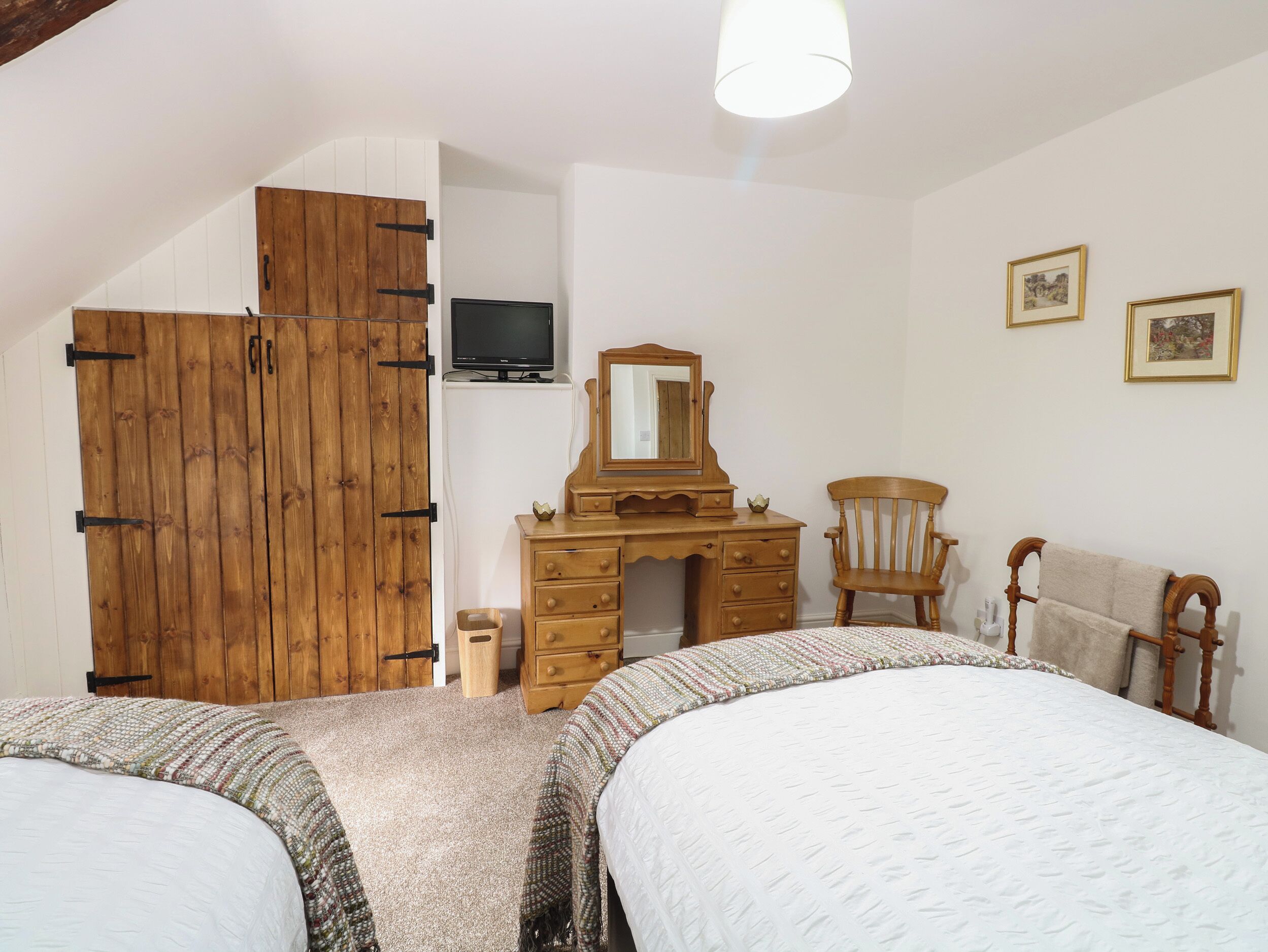 A bedroom with two beds, a wooden wardrobe, a dresser with a mirror, a television, and two framed pictures on the wall.