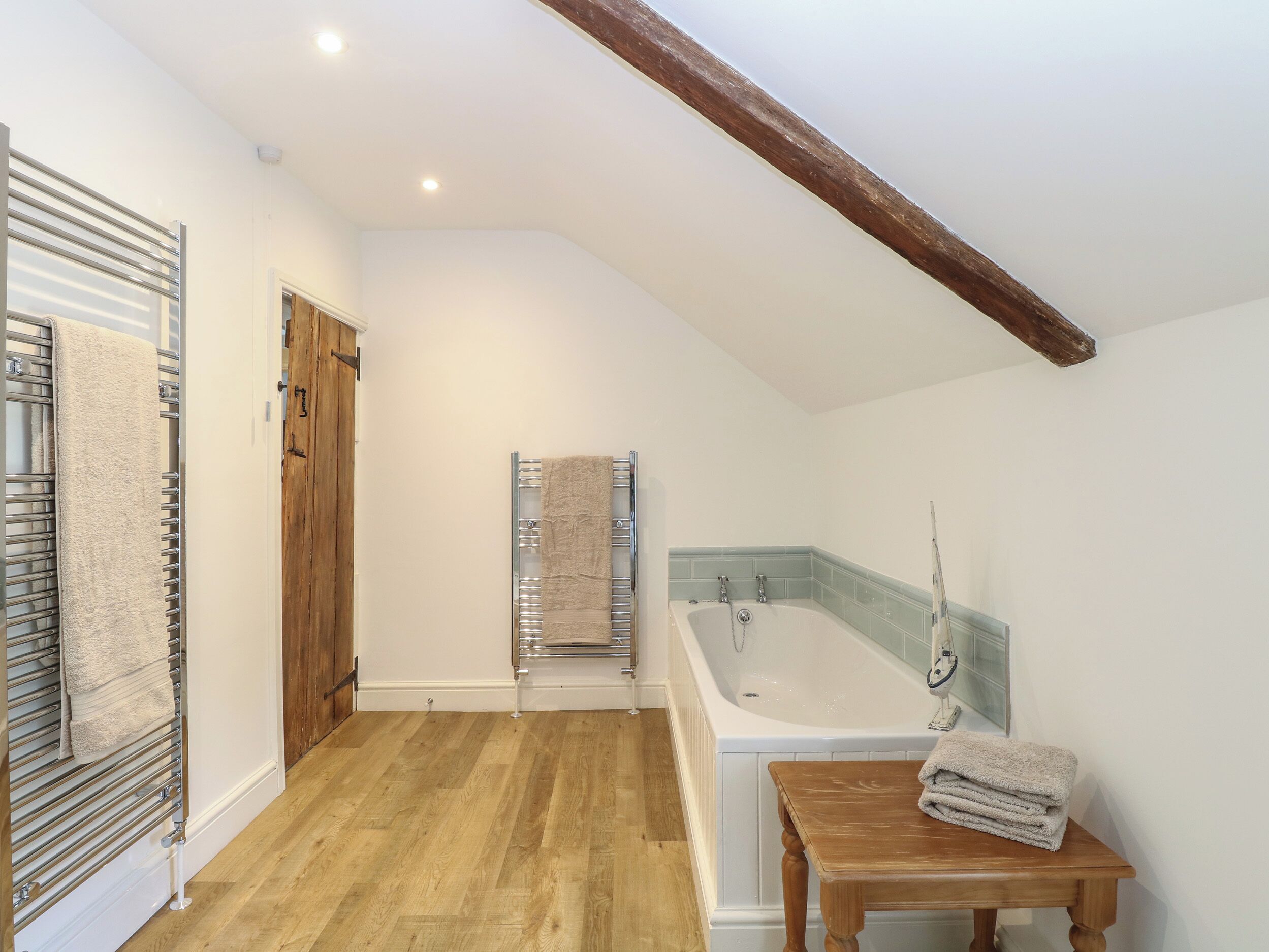 Un baño con suelo de madera, una bañera, una mesita de madera con toallas y un perchero para toallas.