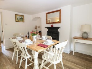 A dining room with a wooden table set for four, white chairs, a fireplace, a mirror, and a lamp on a side table.