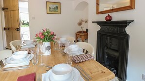 A dining room with a wooden table set for four, a fireplace, and a painting on the wall.