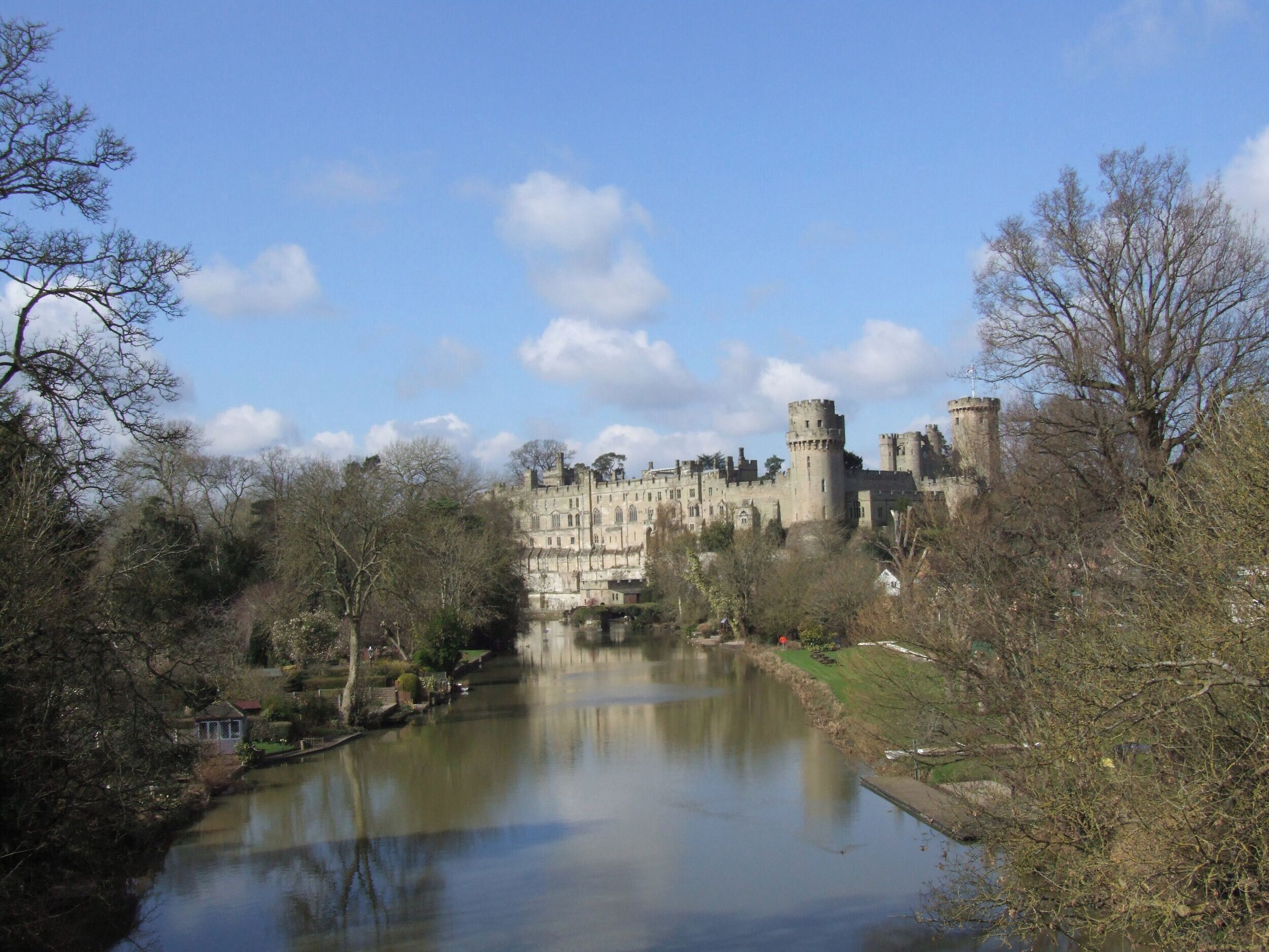 A castle with a moat, surrounded by trees and a clear sky.