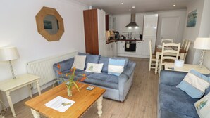 Una sala de estar moderna con un sofá azul, una mesa de centro de madera y un comedor con una mesa y sillas blancas.
