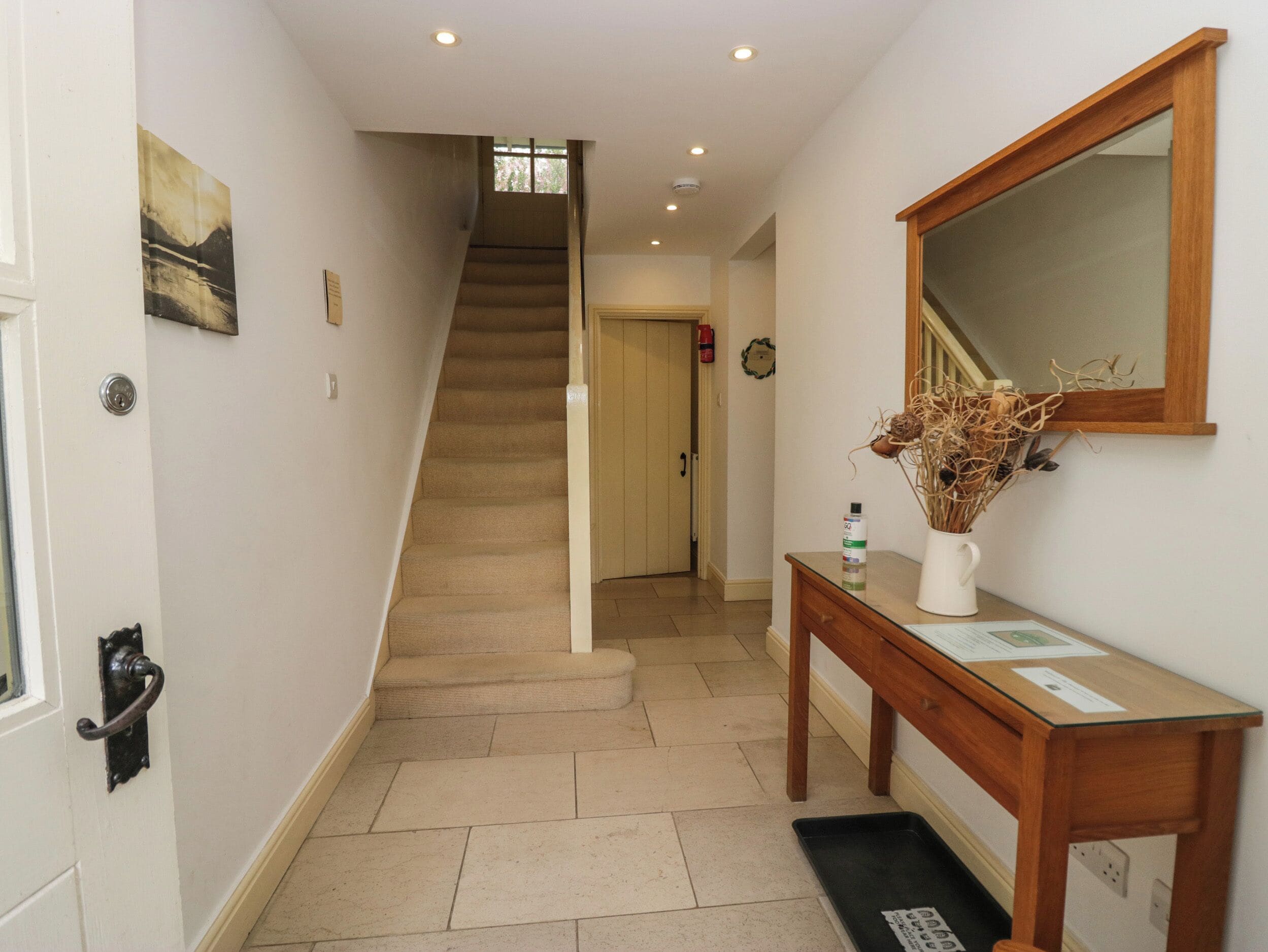 Un pasillo con una escalera alfombrada, una consola de madera con un florero y un espejo en la pared.