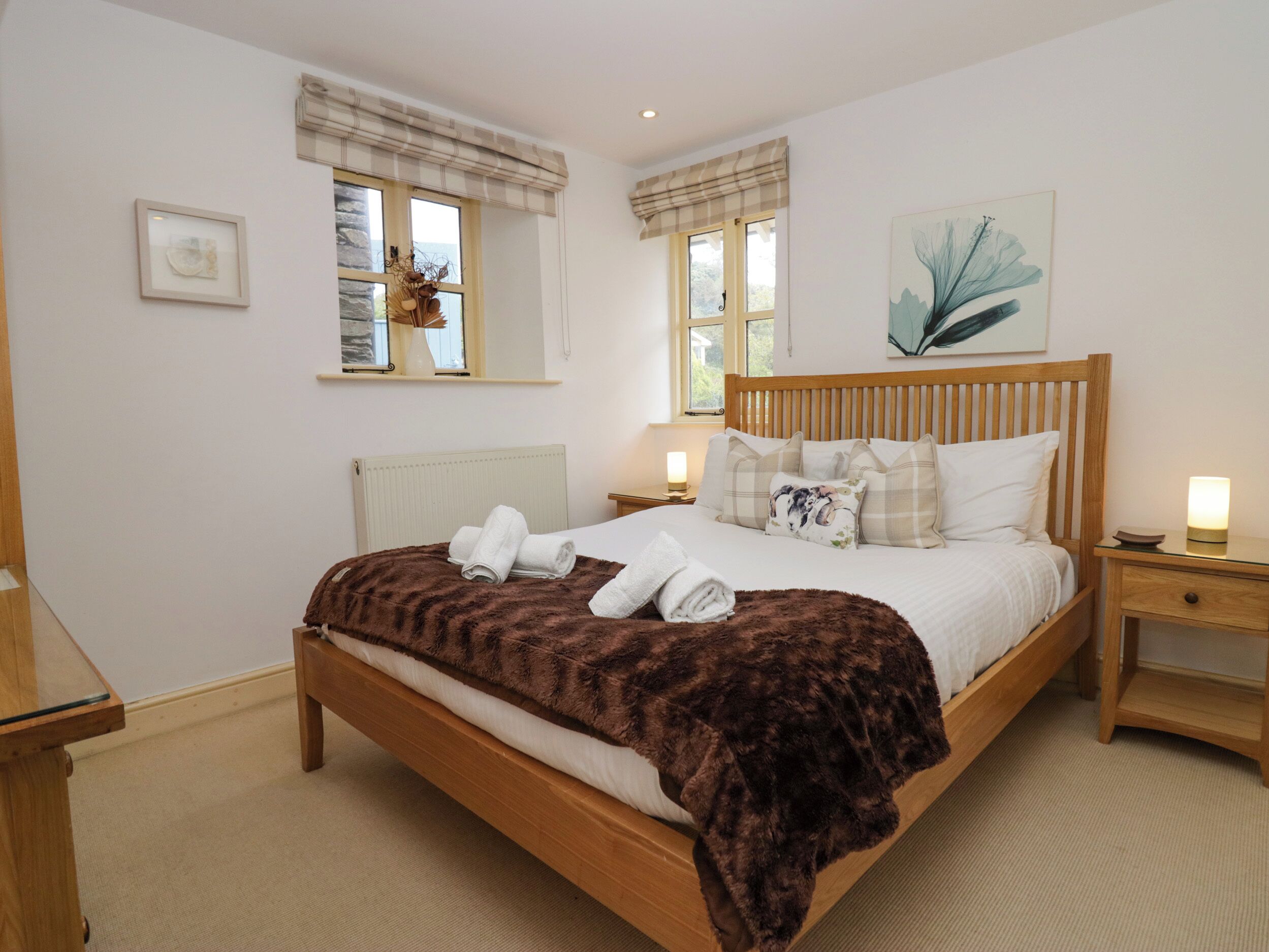 A neatly arranged bedroom with a wooden bed, a bedside table with a lamp, and a window with a view of greenery.