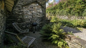 Ein Steinhaus mit rustikalem Äußeren, einer Holzbank und einem Grillbereich.