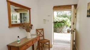 Ein Badezimmer mit einem Holzwaschtisch, einem Spiegel, einer Vase mit Trockenblumen und einer Tür zu einem Garten.
