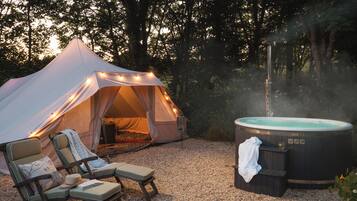 Ein Zelt mit Lichterketten, einem Whirlpool und Liegestühlen in einer Waldlandschaft.