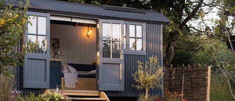 A cozy cabin with a wooden interior, a small porch, and a garden area with potted plants and flowers.