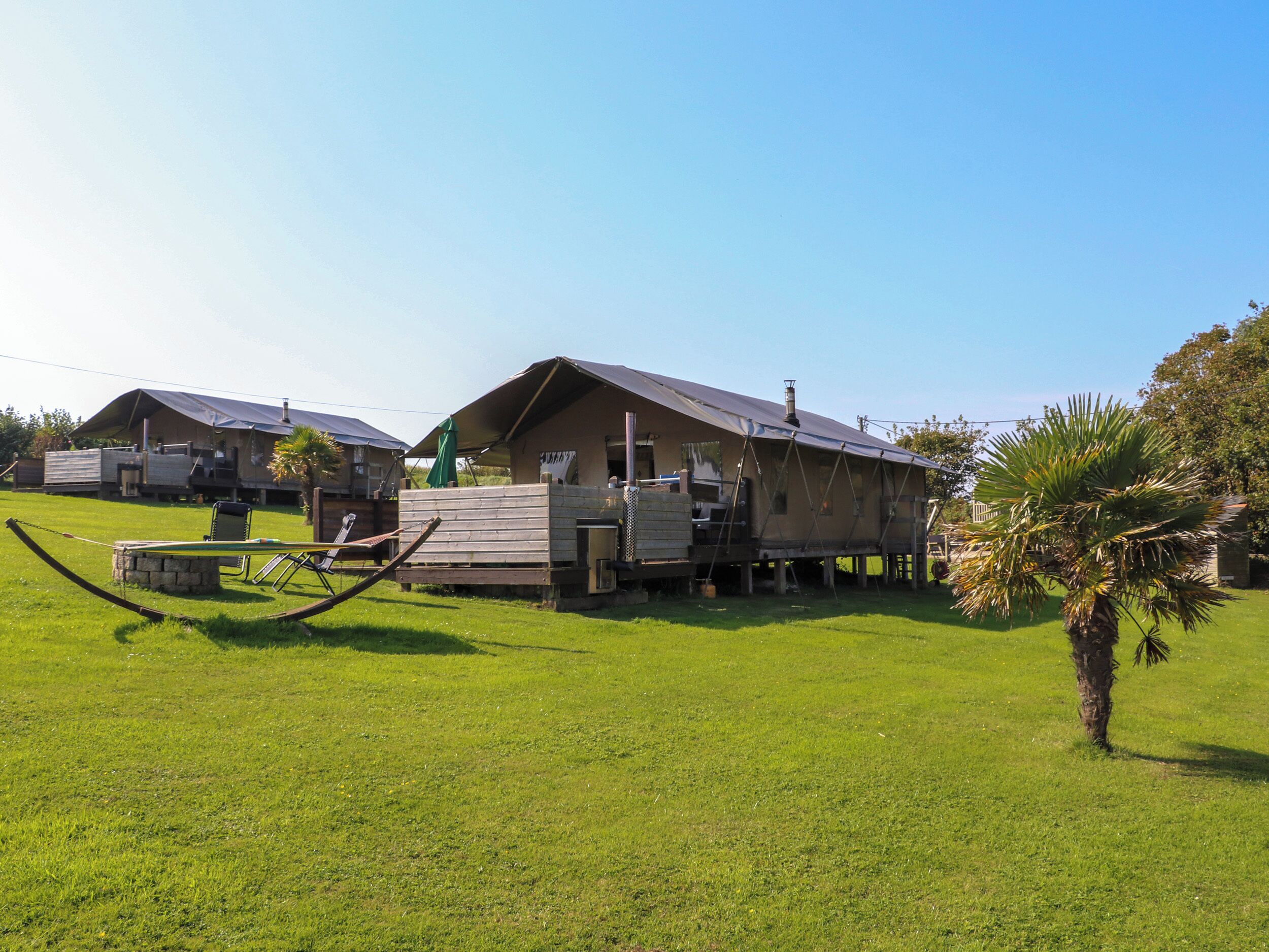 A rustic cabin-style building with a sloped roof and a chimney, surrounded by a well-maintained lawn and a palm tree.