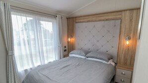 Ein Schlafzimmer mit einem großen Bett, einem Holzkopfende, zwei Nachttischlampen und einem Fenster mit Vorhängen.