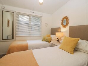 Camera d'albergo con due letti, uno specchio, una lampada a parete e una finestra con persiane.