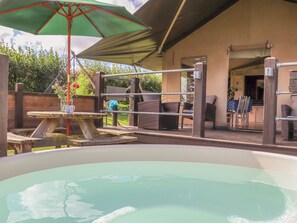 An outdoor hot tub area with a table and chairs under a shaded umbrella, surrounded by wicker furniture and a wooden fence. - Bluebell (Penzance)
