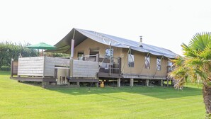 A rustic, single-story building with a sloped roof, a wooden deck, and a small attached structure. - Bluebell (Penzance)