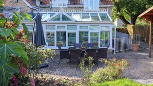A conservatory with a glass roof, wicker furniture, and a stone building with a tiled roof. - The Cheesehouse (Dorchester)