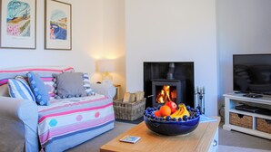 Un salon chaleureux avec un canapé, une table basse sur laquelle se trouve un panier de fruits, une cheminée et un téléviseur.