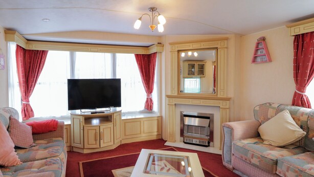 A living room with a flat-screen TV, a fireplace, and two sofas with floral upholstery. - Meric Stone Holiday Lets Caravan 1 (Limavady)