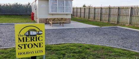 A holiday let named 'The Merc Stone' with a small building, a picnic table, and a fenced area.