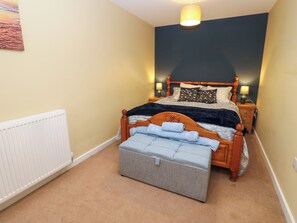 Une chambre à coucher avec un lit, des lampes de chevet, un radiateur et un petit pouf.