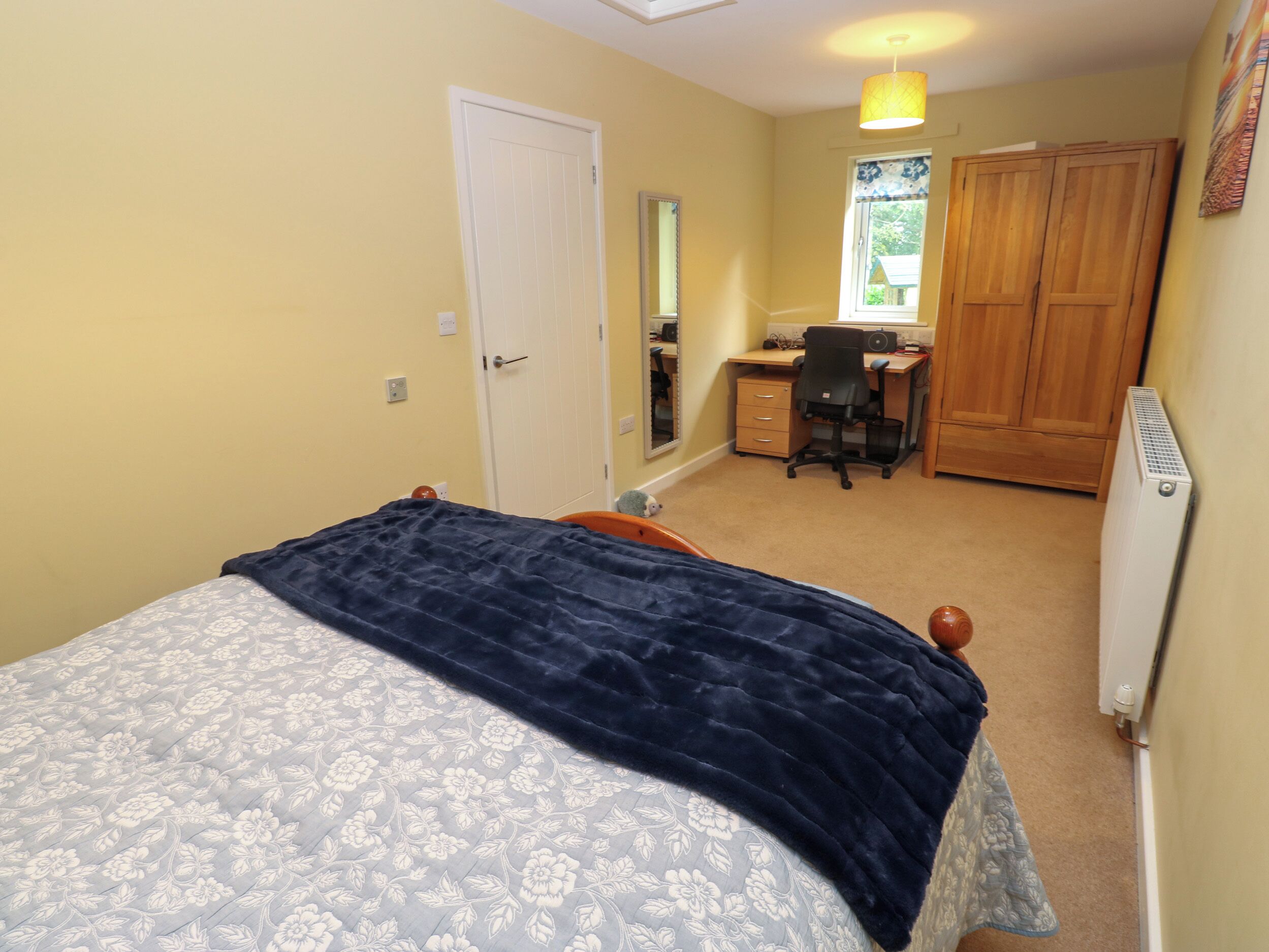 Ein Schlafzimmer mit Bett, Schreibtisch, Stuhl, Kleiderschrank und Heizkörper.