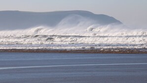 A beach with waves crashing onto the shore and a distant mountain range. - Bay (Ilfracombe)