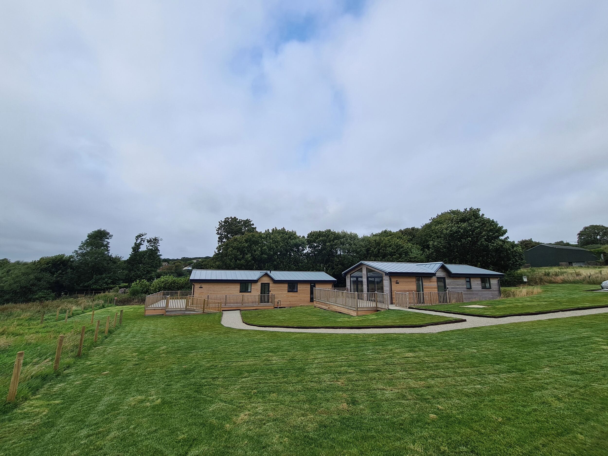A row of modern, single-story cabins with a metal roof, surrounded by a well-maintained lawn and a wooden fence.
