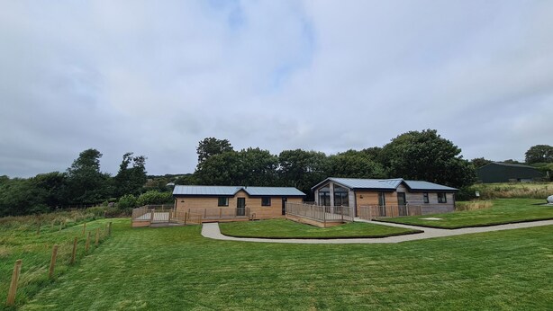 A row of modern, single-story cabins with a metal roof, surrounded by a well-maintained lawn and a wooden fence. - Bay (Ilfracombe)