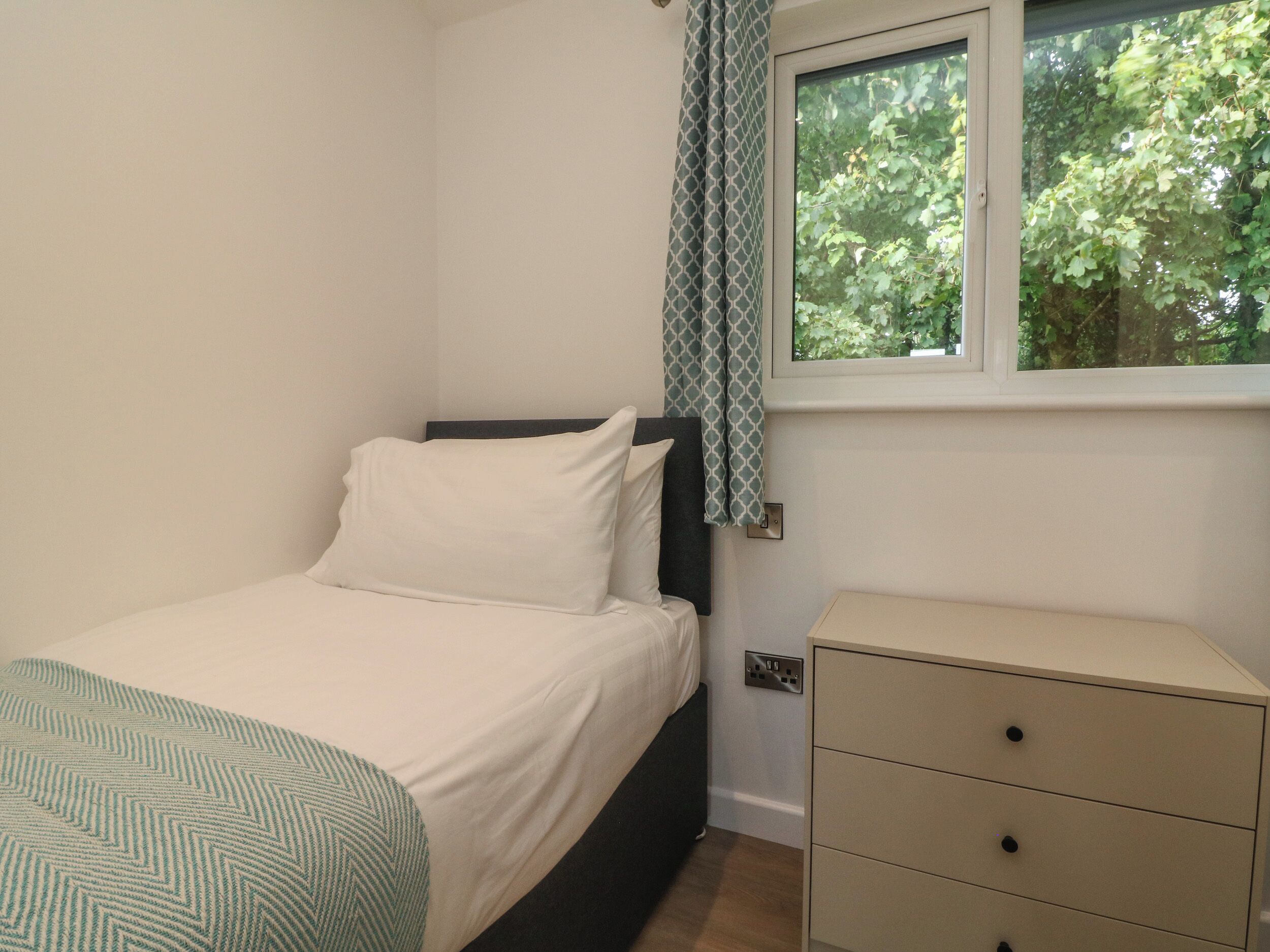 A bedroom with a bed, a bedside table, and a window with a view of trees.