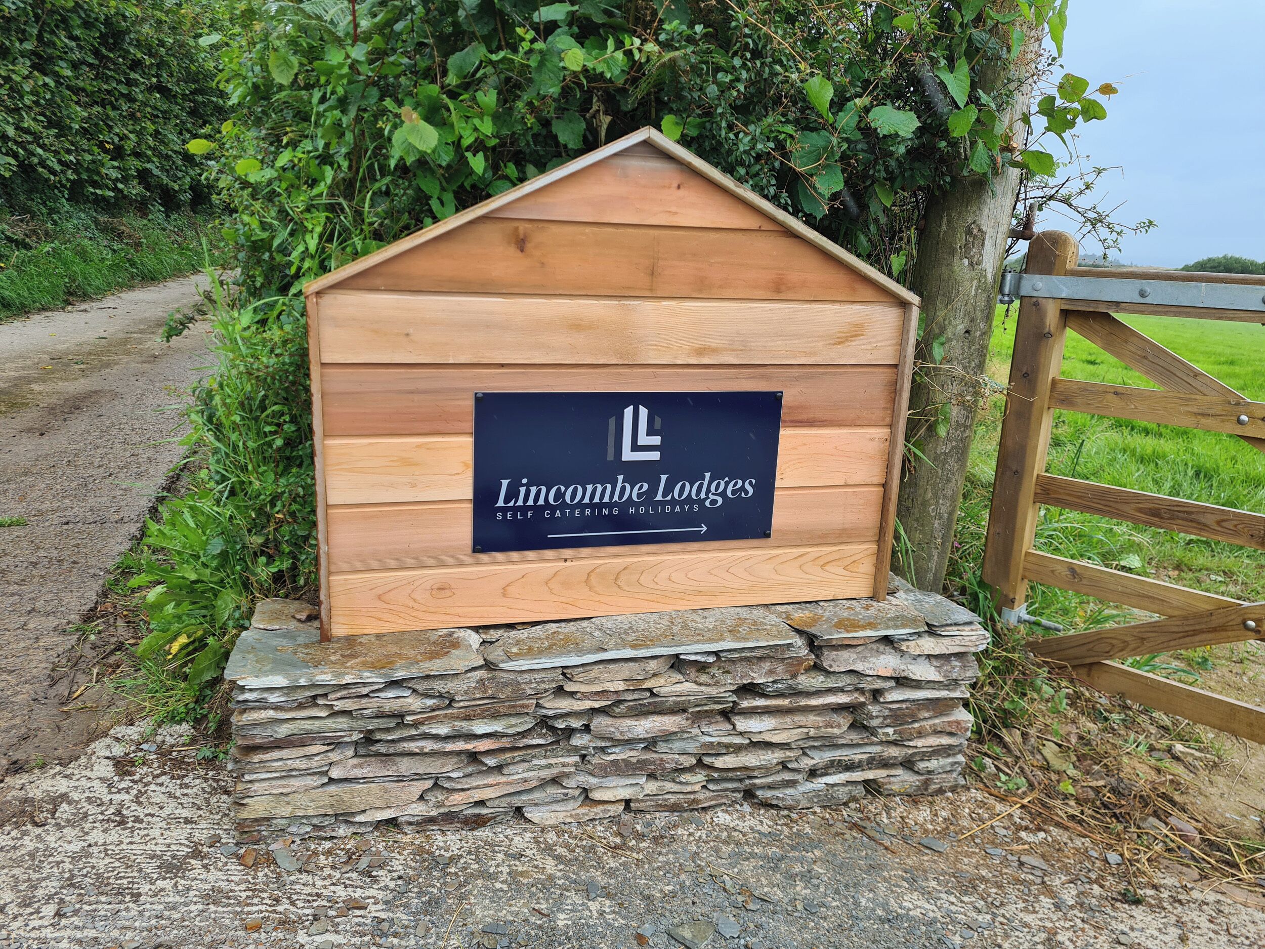 Un panneau en bois indiquant l’emplacement de Lincombe Lodges et proposant des locations de vacances avec possibilité de cuisiner soi-même.