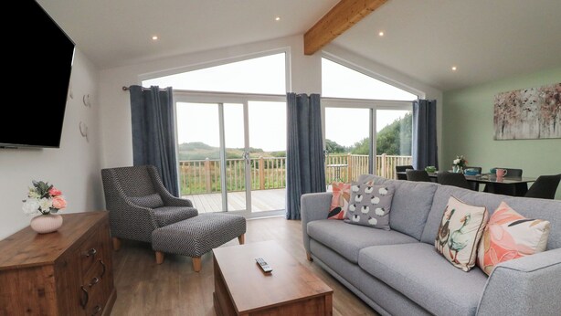A spacious living room with a grey sofa, patterned armchair, and wooden coffee table. - Bay (Ilfracombe)