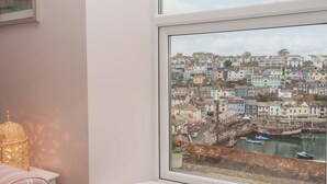 A bedroom with a large window overlooking a coastal town. - The White House (Brixham)