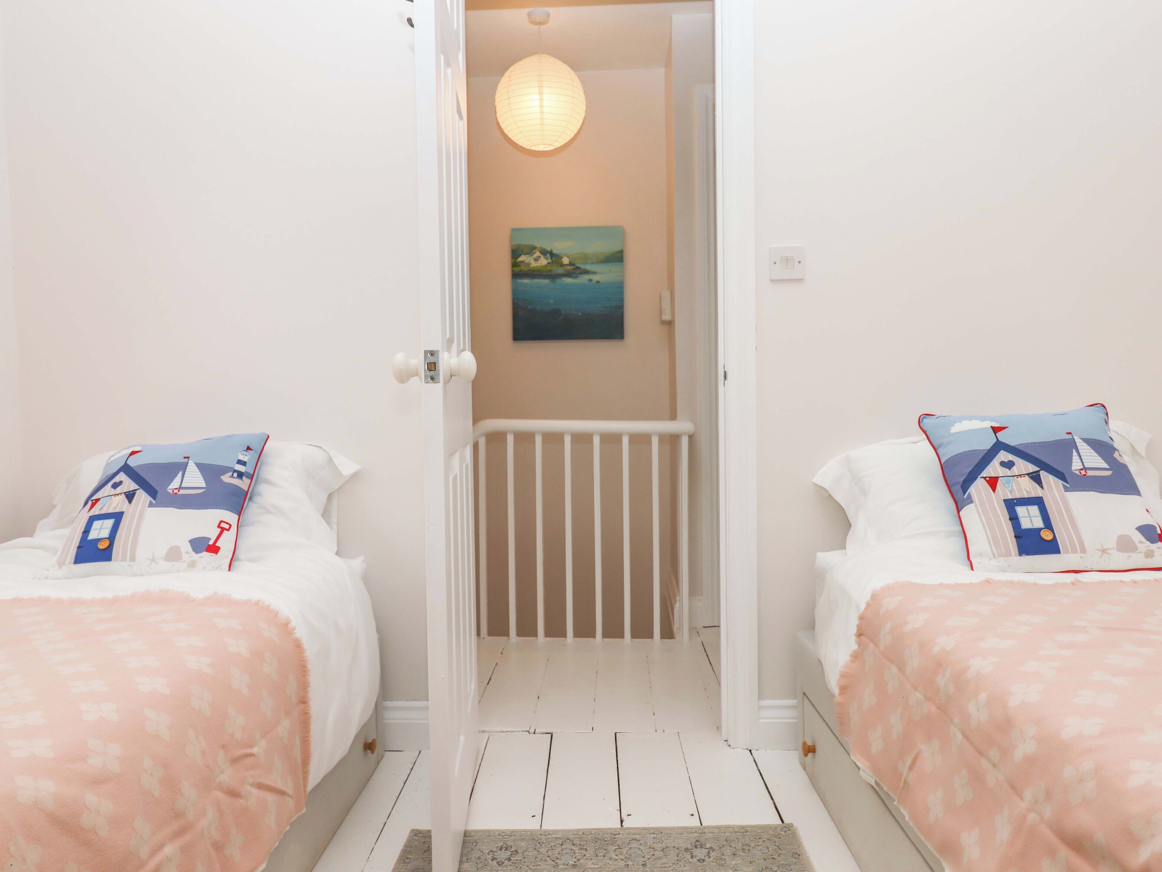 Un dormitorio con dos camas, cada una con almohada a juego, una cuna blanca en el centro y un cuadro en la pared.