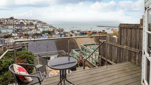A balcony with a table and chairs, overlooking a coastal town with colorful buildings and boats in the water. - The White House (Brixham)