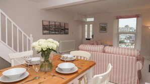 A dining area with a wooden table set for four, white chairs, and a vase of white flowers. A striped sofa is visible in the background. - The White House (Brixham)