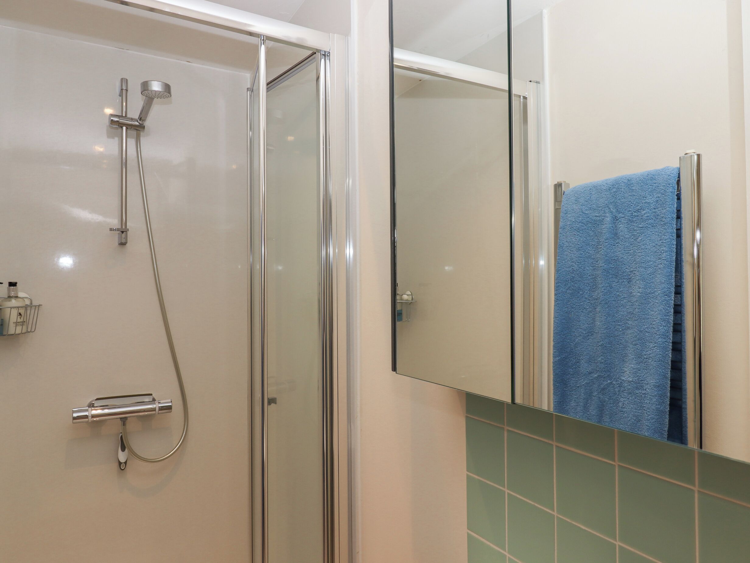 Een douche met glazen wanden, een handdouche en een kraan op de muur.