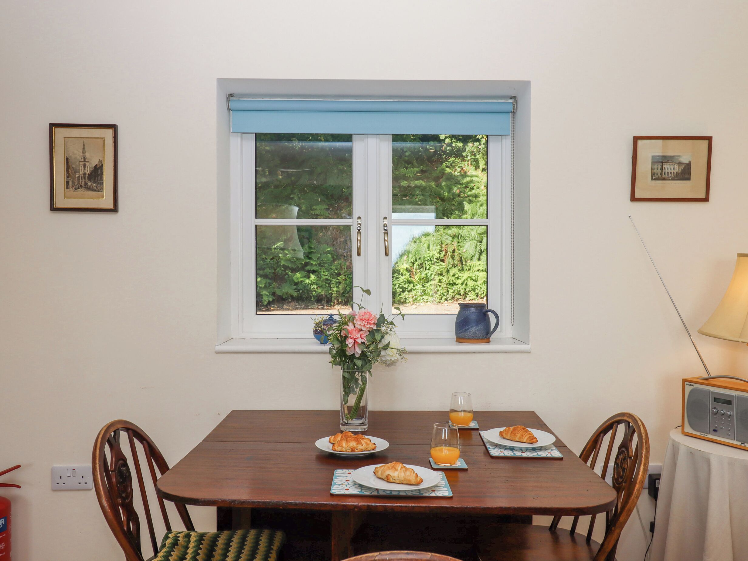 Un coin repas avec une table mise pour le petit-déjeuner, une fenêtre donnant sur un paysage verdoyant et une radio posée sur une table d’appoint.
