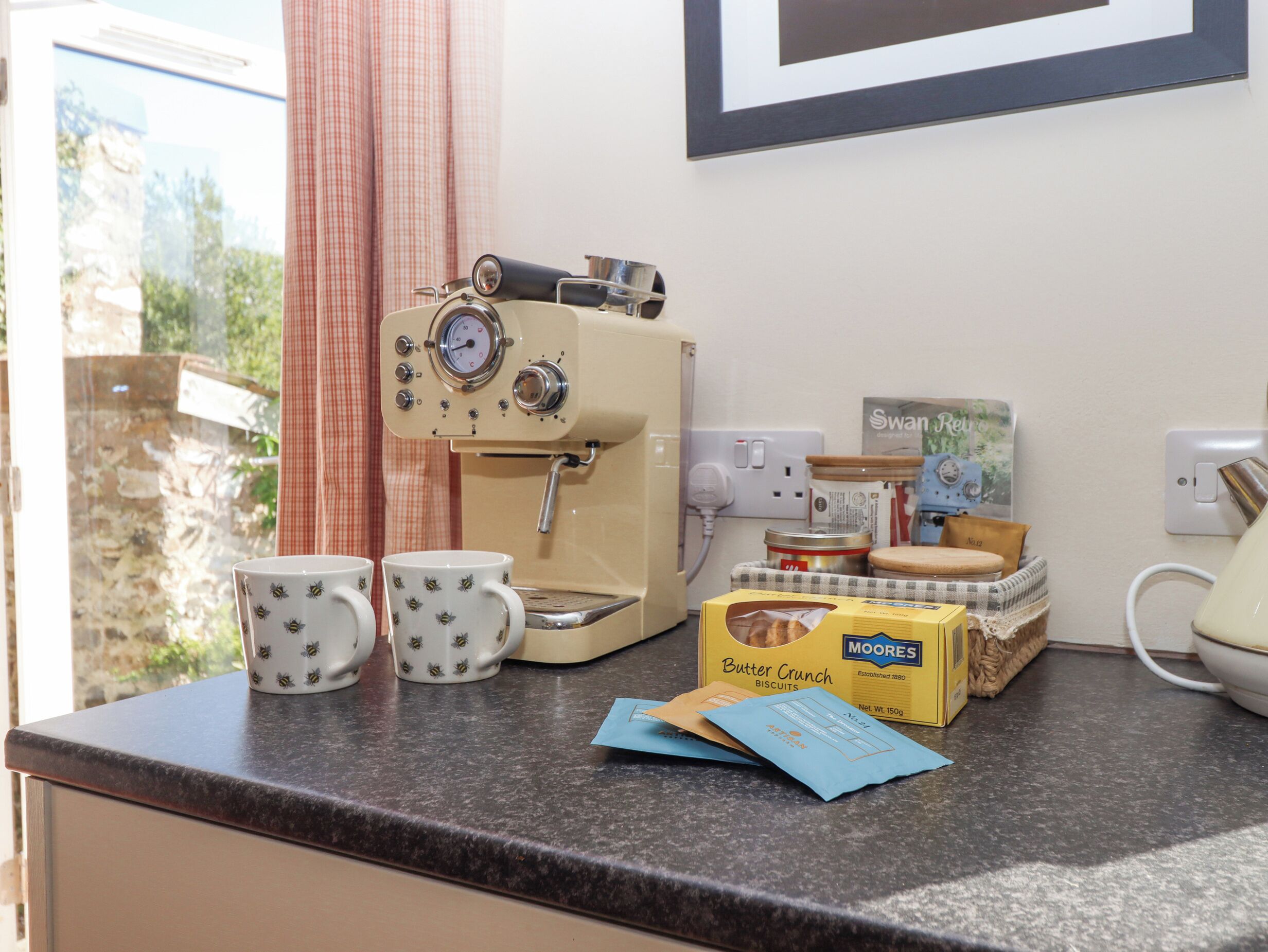 A kitchen counter with a coffee machine, two mugs, a box of biscuits, and a kettle.