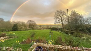 Paesaggio rurale con arcobaleno, campi verdi e un muro di pietra.