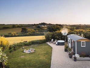 A rustic cabin with a hot tub, surrounded by a gravel path, lush greenery, and a view of rolling hills. - Stargazer (Truro)
