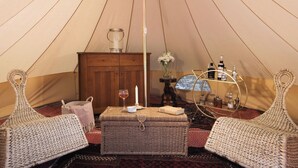 Een gezellig ingerichte tent met een houten kast, een tafel met een kaars en rieten meubels.