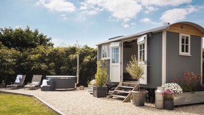 Een klein, laag huis met een veranda, een jacuzzi en een tuin met bloempotten en bloemen.