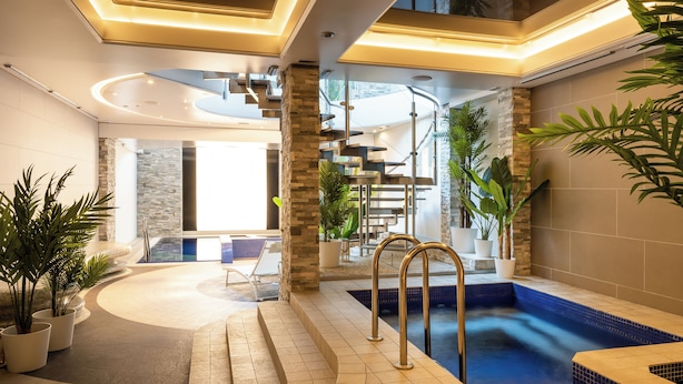 A modern indoor pool area with a spa, stone pillars, and potted plants. - Coco Boutique Hotel & Spa  (Karpacz)