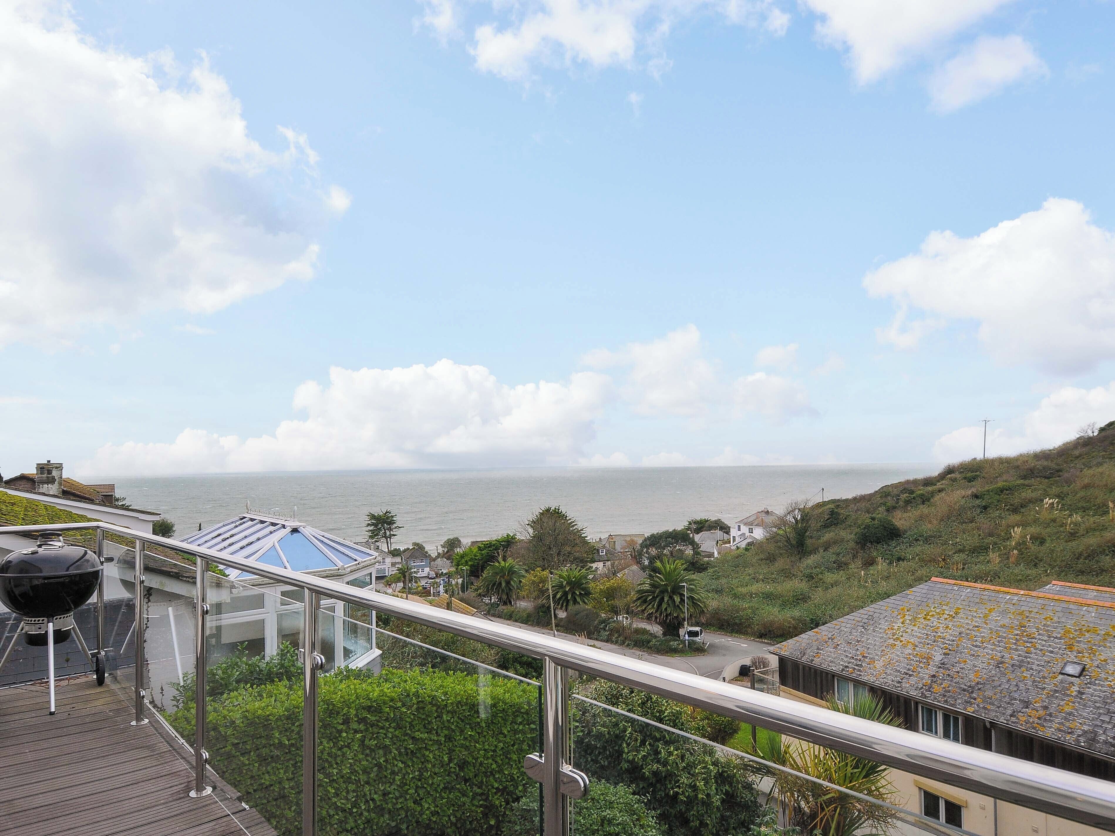 Uitzicht op de kust vanaf een balkon, met heldere lucht, zee en omliggende begroeiing.