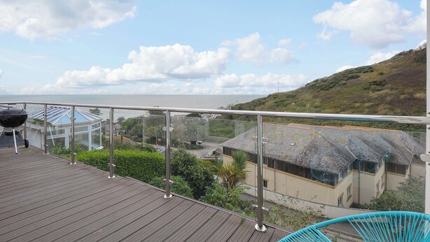 Un balcone con vista sul mare, un edificio con tetto di paglia e una casa moderna con tetto in vetro.